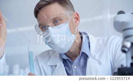 Man with safety glasses and blue mask is working with lab tubes using a pipette in a modern laboratory, close-up of researcher. Science and medicine Man with safety glasses and blue mask is working with lab tubes using a pipette in a modern laboratory, close-up of researcher. Science and medicine 122955714