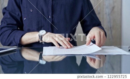 Businessman in dark blue t-shirt analyzing document at desk. Close-up of a professional auditor or lawyer reviewing a lengthy paper report in office setting. Business people concept 122955725