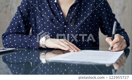 Businesswoman is signing corporate contract at her office desk in formal dark blue blouse with polka dots. Business people concept 122955727