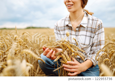 A woman agronomist studies the golden harvest of wheat on an agricultural field. Agriculture. 122955736