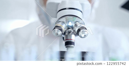 Professional scientist in protective gear is using microscope in a laboratory setting, close-up. Science and medicine concepts Professional scientist in protective gear is using microscope in a laboratory setting, close-up. Science and medicine concepts 122955742