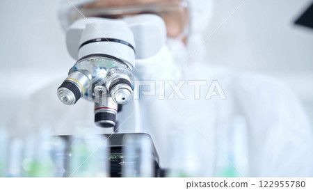 Professional scientist in protective gear is using microscope in a laboratory setting, close-up. Science and medicine concepts 122955780
