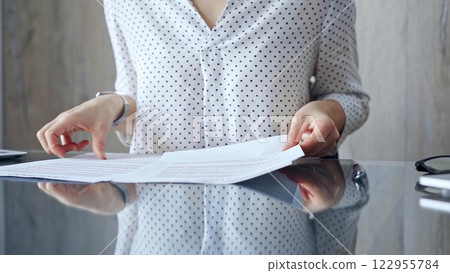 Auditor woman analyzing financial documents with magnifying glass and calculator at her office desk in formal dark blue blouse with polka dots. Business people concept 122955784