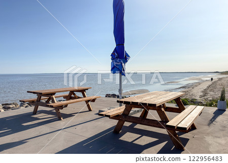 Relaxing seaside picnic spot with wooden benches and a closed blue umbrella 122956483
