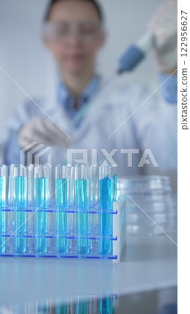 Test tubes with a blue liquid, close-up view. Scientist holding pipette conducting experiments in laboratory on the background. Science and Medicine Test tubes with a blue liquid, close-up view. Scientist holding pipette conducting experiments in laboratory on the background. Science and Medicine 122956627