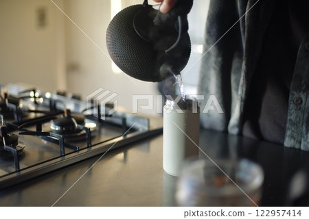Pouring boiled water from an iron kettle into a water bottle Pouring boiled water from an iron kettle into a water bottle 122957414