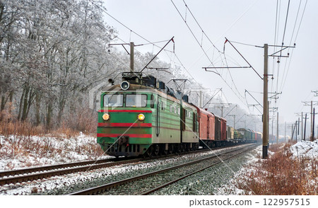 Old Soviet electric locomotive with a long freight train in winter in Kyiv Oblast of Ukraine 122957515