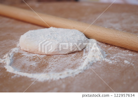 Rolling dough on a wooden surface with flour scattered around 122957634