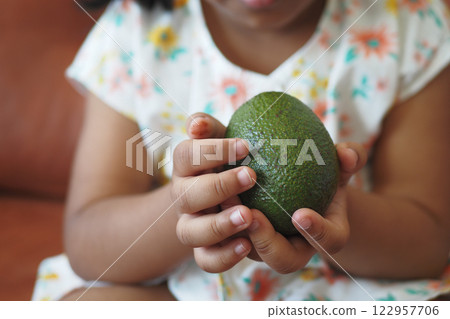 Child holds fresh avocado in hands while sitting indoors 122957706