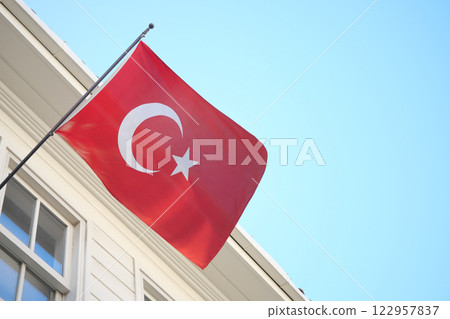 Turkish flag waving against a clear blue sky in front of a building 122957837
