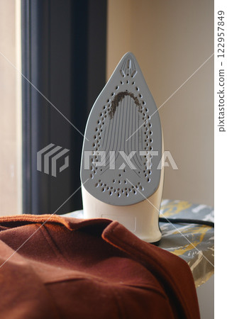 Iron resting on fabric near a window in a bright room 122957849