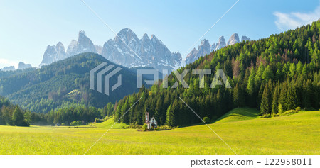 Scenic alpine landscape with church and majestic mountain peaks in verdant valley near Valley of Funes at Dolomites, Italy 122958011