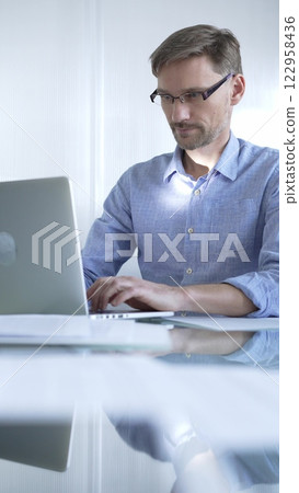 Casual dressed businessman is using a laptop in a contemporary office, with a clean, bright environment that boosts efficiency. Business people concept Casual dressed businessman is using a laptop in a contemporary office, with a clean, bright environment that boosts efficiency. Business people concept 122958436
