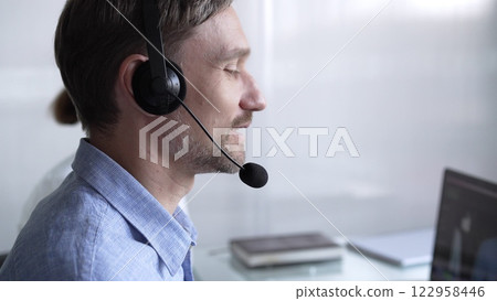 Happy smiling male call center operator in blue casual shirt is assisting clients online, providing customer support and answering inquiries. Business call center 122958446