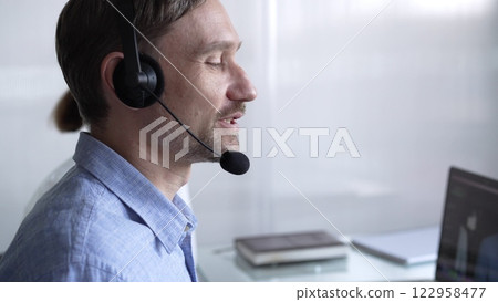 Happy smiling male call center operator in blue casual shirt is assisting clients online, providing customer support and answering inquiries. Business call center Happy smiling male call center operator in blue casual shirt is assisting clients online, providing customer support and answering inquiries. Business call center 122958477