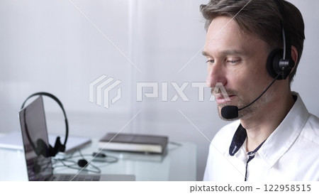 Businessman wearing headset and glasses, using laptop for video conference call, working remotely from home office. Call center concept Businessman wearing headset and glasses, using laptop for video conference call, working remotely from home office. Call center concept 122958515