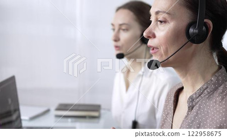 Focused female call center operator in brawn dotted blouse is assisting clients online, providing customer support and answering inquiries. Call center operators 122958675