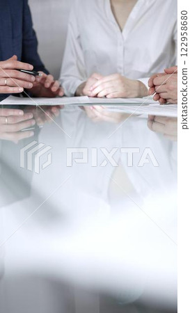 Unrecognizable business people are reviewing contract terms during a meeting while sitting at the glass table in office, vertical close up view. Copy space area Unrecognizable business people are reviewing contract terms during a meeting while sitting at the glass table in office, vertical close up view. Copy space area 122958680