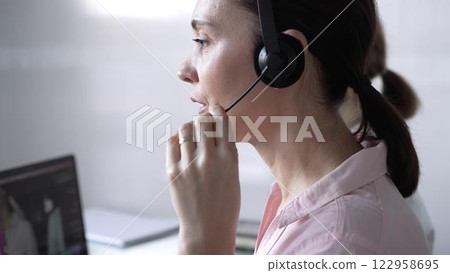 Focused female call center operator in pink casual blouse is assisting clients online, providing customer support and answering inquiries. Business call center Focused female call center operator in pink casual blouse is assisting clients online, providing customer support and answering inquiries. Business call center 122958695