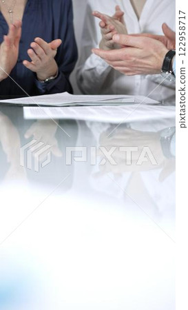 Business people or lawyers are applauding and celebrating achievements at glass table after successful meeting, vertical close up view. Concept of success 122958717