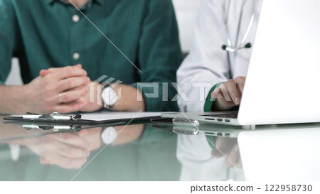 Doctor woman is typing on laptop computer while listening to patient complaints during medical consultation in clinic office. Medicine concept 122958730