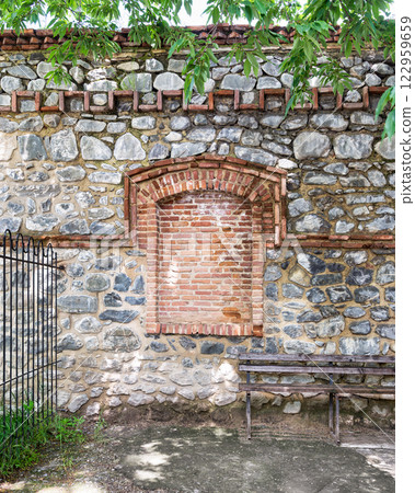 Stone wall with brick arch and wooden bench in a tranquil outdoor space 122959659
