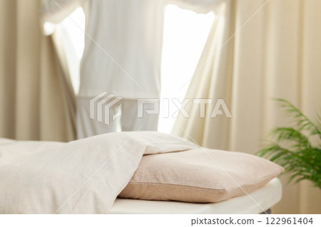 A middle-aged woman in pajamas opening the curtains in her bedroom in the morning A middle-aged woman in pajamas opening the curtains in her bedroom in the morning 122961404