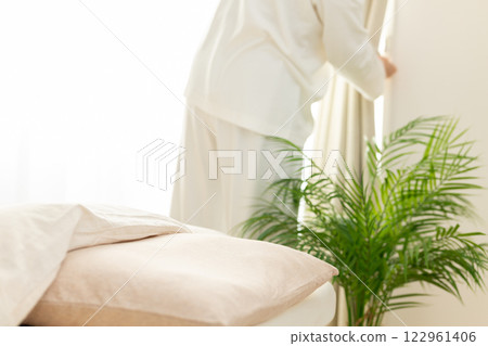 早上，一位穿著睡衣的中年婦女在臥室拉開窗簾 122961406