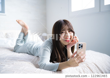 Woman lying down and looking at the camera with a smartphone, full body 122961465