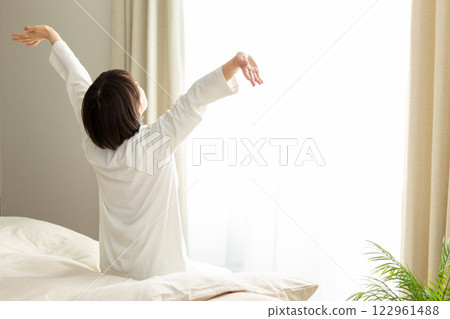一名身穿睡衣的中年婦女清晨在臥室伸展身體 122961488