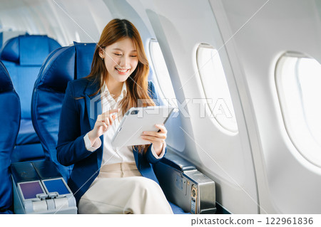 Asian female passenger of airplane sitting in comfortable seat while working laptop and tablet. Travel in style, Asian female passenger of airplane sitting in comfortable seat while working laptop and tablet. Travel in style, 122961836