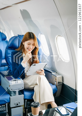 Asian female passenger of airplane sitting in comfortable seat while working laptop and tablet. Travel in style, Asian female passenger of airplane sitting in comfortable seat while working laptop and tablet. Travel in style, 122961837