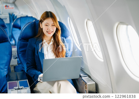 Asian female passenger of airplane sitting in comfortable seat while working laptop and tablet. Travel in style, Asian female passenger of airplane sitting in comfortable seat while working laptop and tablet. Travel in style, 122961838