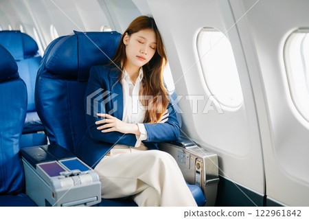 Asian female passenger of airplane sitting in comfortable seat while working laptop and tablet. Travel in style, 122961842