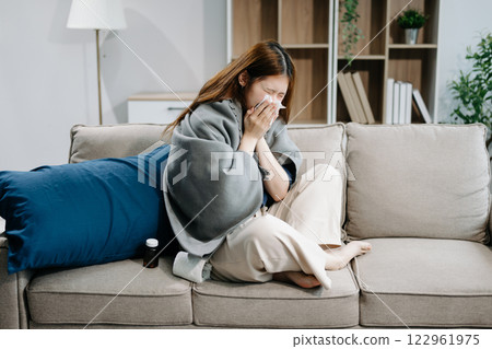 Young Asian woman suffering from flu symptoms, covered with a blanket on a sofa. Concept of illness, healthcare Young Asian woman suffering from flu symptoms, covered with a blanket on a sofa. Concept of illness, healthcare 122961975