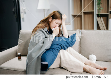 Young Asian woman suffering from flu symptoms, covered with a blanket on a sofa. Concept of illness, healthcare 122961978