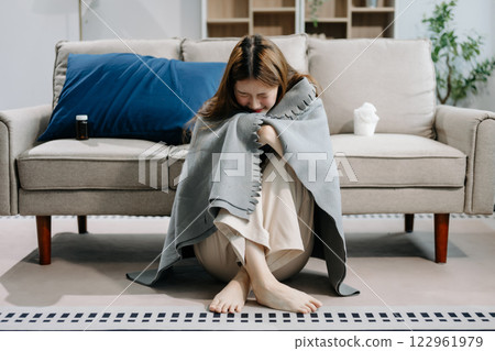 Young Asian woman suffering from flu symptoms, covered with a blanket on a sofa. Concept of illness, healthcare 122961979
