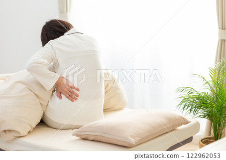 一名身穿白色睡衣的中年婦女早上在臥室裡感到背痛 122962053