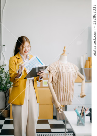 Asian tailor woman working on clothes in tailoring atelier. beautiful young female fashion designer smile Asian tailor woman working on clothes in tailoring atelier. beautiful young female fashion designer smile 122962335