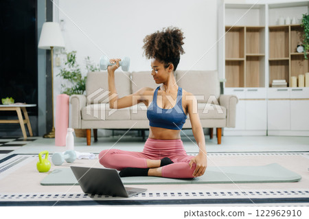Woman Doing Yoga and Watching Online Tutorials on Laptop, Training in Living Room at home Woman Doing Yoga and Watching Online Tutorials on Laptop, Training in Living Room at home 122962910