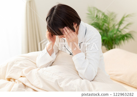 一名身穿白色睡衣的中年婦女早上在臥室頭痛 一名身穿白色睡衣的中年婦女早上在臥室頭痛 122963282