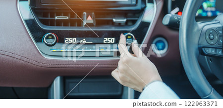 Woman hand adjusting temperature the air flowing during driving car on the road, air conditioner cooling system inside the car. Adjust, temperature and transport concept 122963371