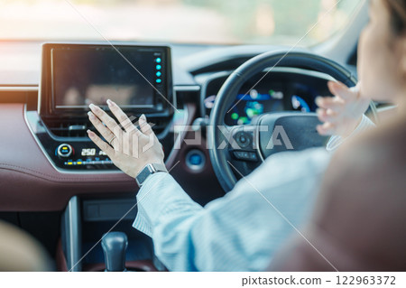 Woman hand adjusting temperature the air flowing during driving car on the road, air conditioner cooling system inside the car. Adjust, temperature and transport concept 122963372