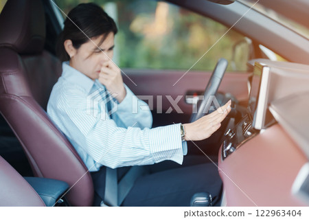 Asian woman hold nose because bad smell after turn on air conditioning in car. Woman driving car with broken air conditioning in hot summer weather. Businesswoman driver is tired, overheat and stress 122963404