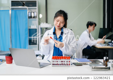 Confident young asian female doctor in white medical uniform sit at desk working on computer. Confident young asian female doctor in white medical uniform sit at desk working on computer. 122963421