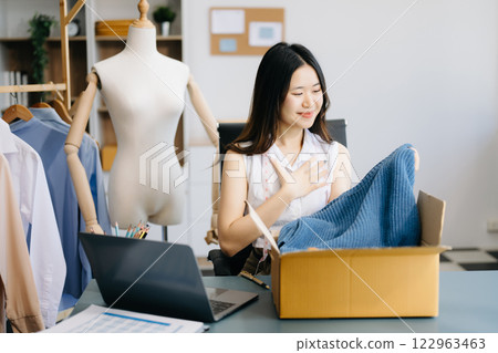 Asian lady blogger showing clothes in front of the camera to recording vlog video live streaming at her shop. Asian lady blogger showing clothes in front of the camera to recording vlog video live streaming at her shop. 122963463