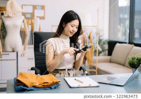 Asian tailor woman working on clothes in tailoring atelier. beautiful young female fashion designer smile and after success in studio 122963473