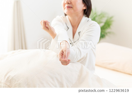 一名身穿白色睡衣的中年婦女早上在臥室伸展身體 一名身穿白色睡衣的中年婦女早上在臥室伸展身體 122963619