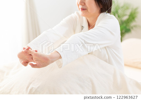 一名身穿白色睡衣的中年婦女早上在臥室伸展身體 122963627