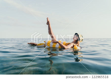 Woman Inflatable Ring Ocean Summer: A woman wearing sunglasses floats on an inflatable ring in the ocean during the summer. 122965518